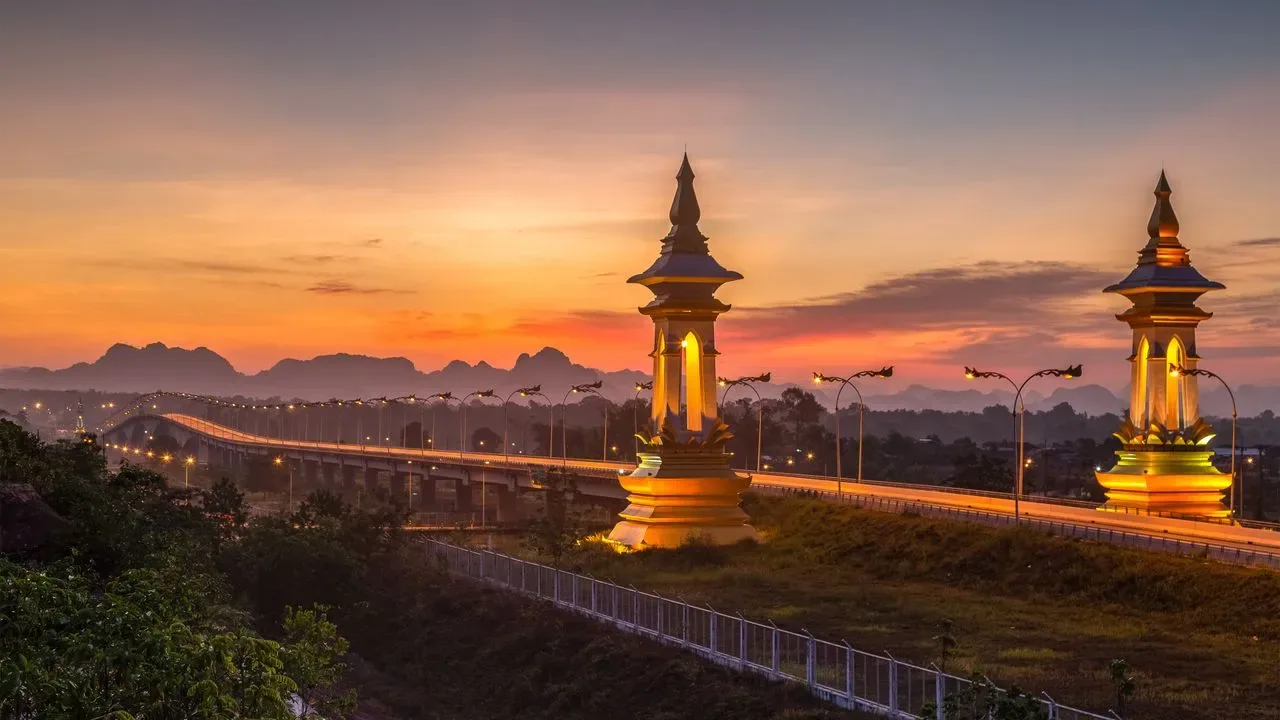 A Thai-Lao Friendship Bridge over the Mekong at dusk, with a gilded Lao boundary marker in the foreground
