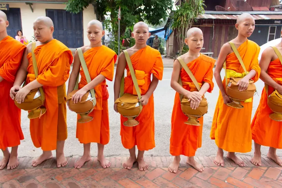 Novizen in safranfarbenen Roben auf einer Strasse in Luang Prabang